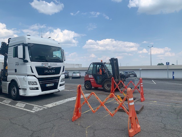 Camion MAN et chariot élévateur près d'une balance Ademi Pesage sous un ciel dégagé.